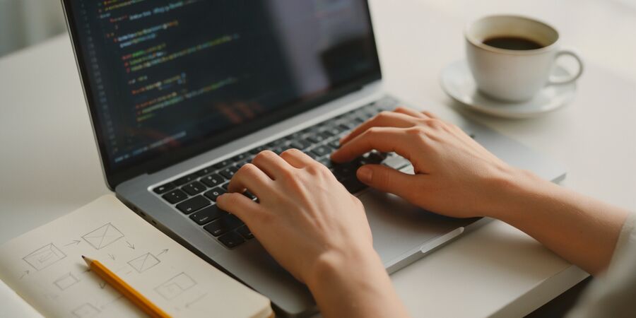 Hands on a laptop showing code, coffee beside